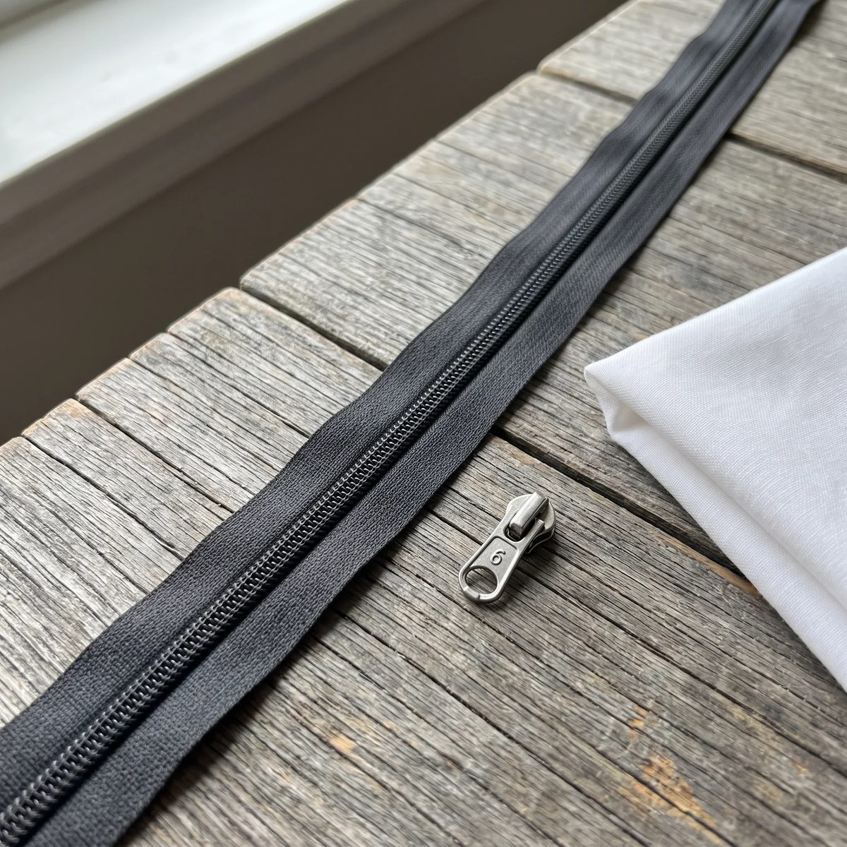 Cremallera continua número 6 gris oscuro sobre una mesa de taller, con el deslizador suelto al lado