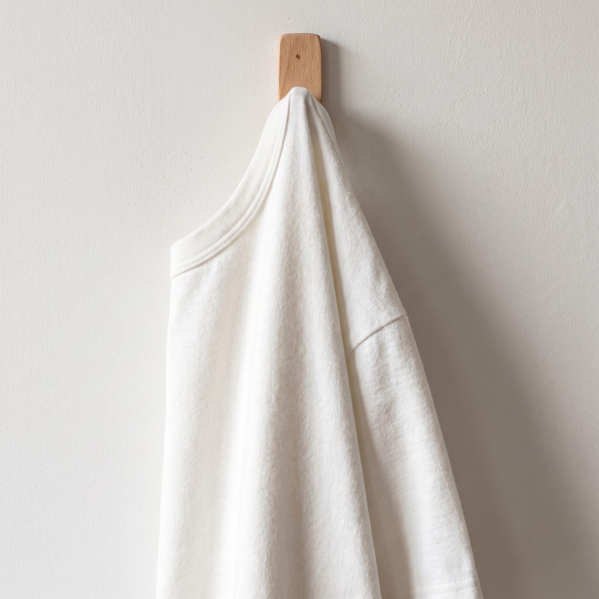 Camiseta blanca en franela pesada colgada en un gancho de madera, Textti