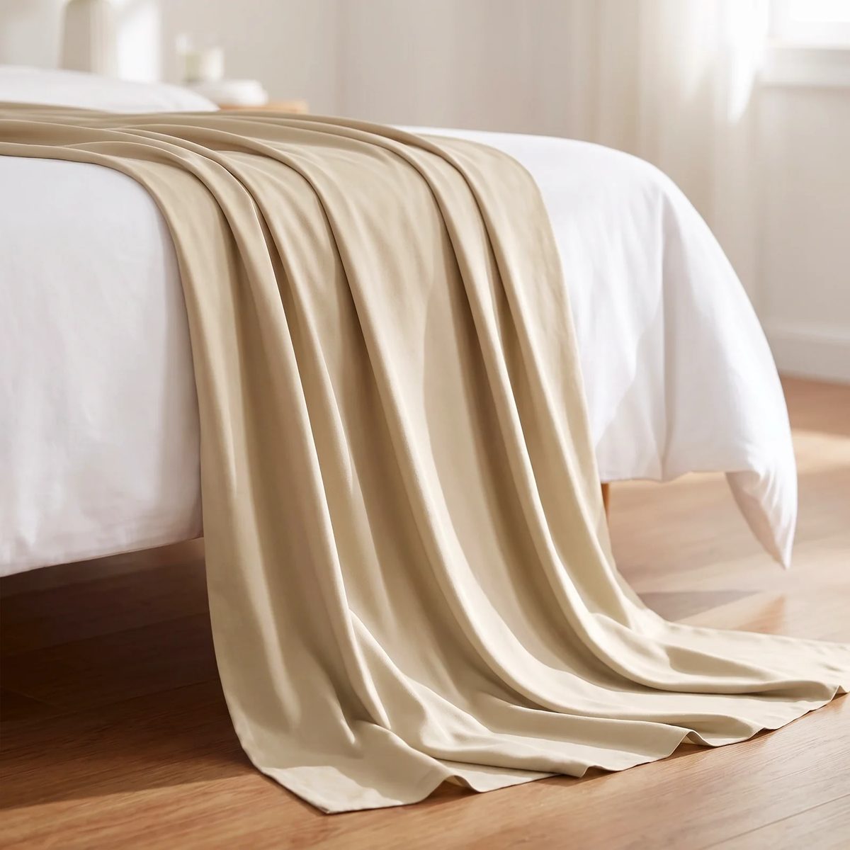 Rayón de bambú color beige, la tela cayendo desde la esquina de una cama, con la luz de la mañana