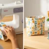 Proceso de cómo hacer bolsas de tela: manos cosiendo un asa en una máquina, con bolsas terminadas al lado.